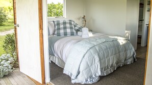 A bedroom with a bed, a bedside table, a lamp, and a window. - Herb Cottage (Haumoana)