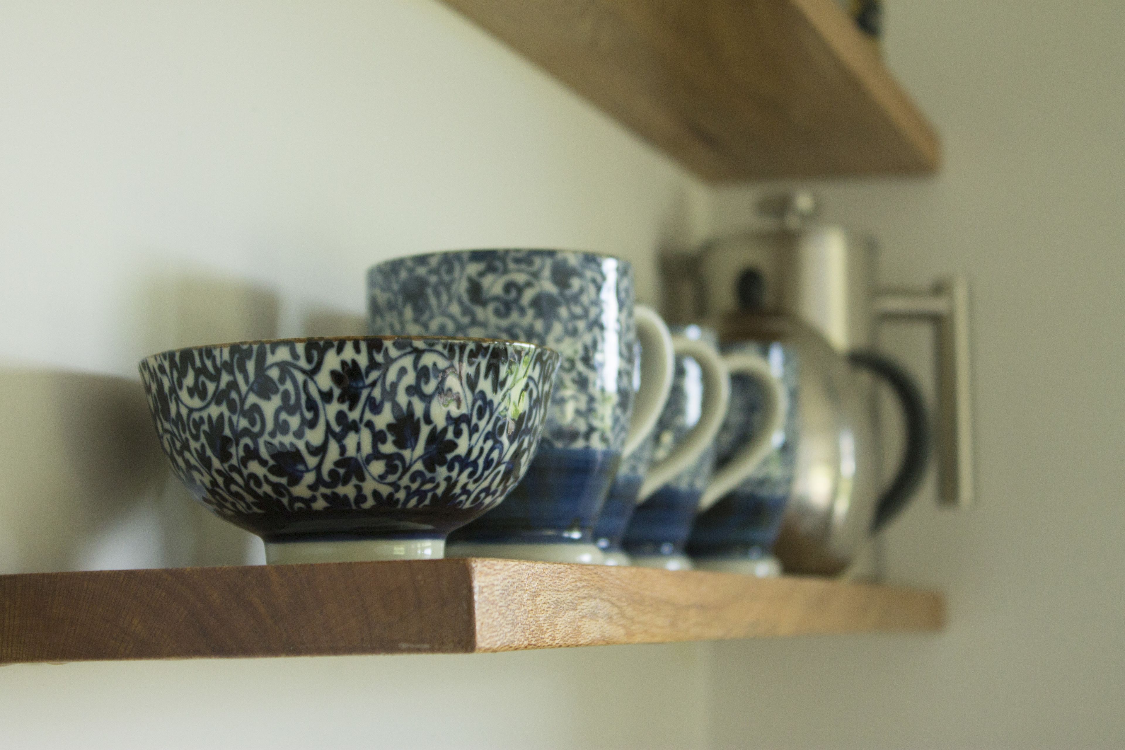 A shelf with a blue and white patterned bowl, a matching cup, and a silver teapot.