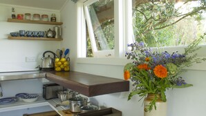 A kitchen with wooden shelves, a window, and a vase with flowers. - Herb Cottage (Haumoana)
