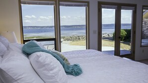 Un dormitorio con una cama grande, ropa de cama blanca y vistas al mar a través de amplias ventanas.