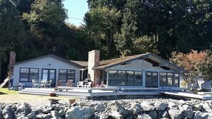 Una casa de dos pisos con un patio, ventanas amplias y cimientos de piedra.