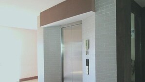 Een moderne lift met een metalen afwerking, een intercom bevestigd aan de muur en een deur met een handgreep.