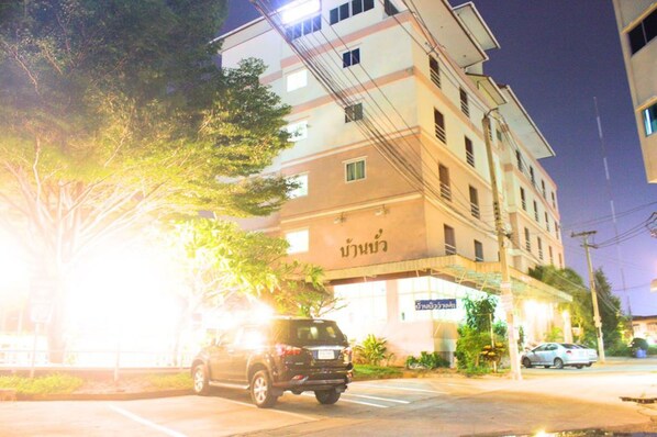 A multi-story building with a sign in a foreign language, parked cars, and trees. - Ban Bua Resort & Hotel (Khon Kaen)
