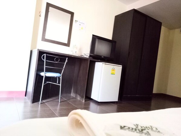 A compact hotel room with a desk, a small refrigerator, a chair, and a television.