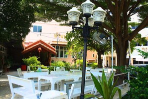 Un espace extérieur aménagé avec des tables et des chaises blanches, un lampadaire et un bâtiment en arrière-plan.