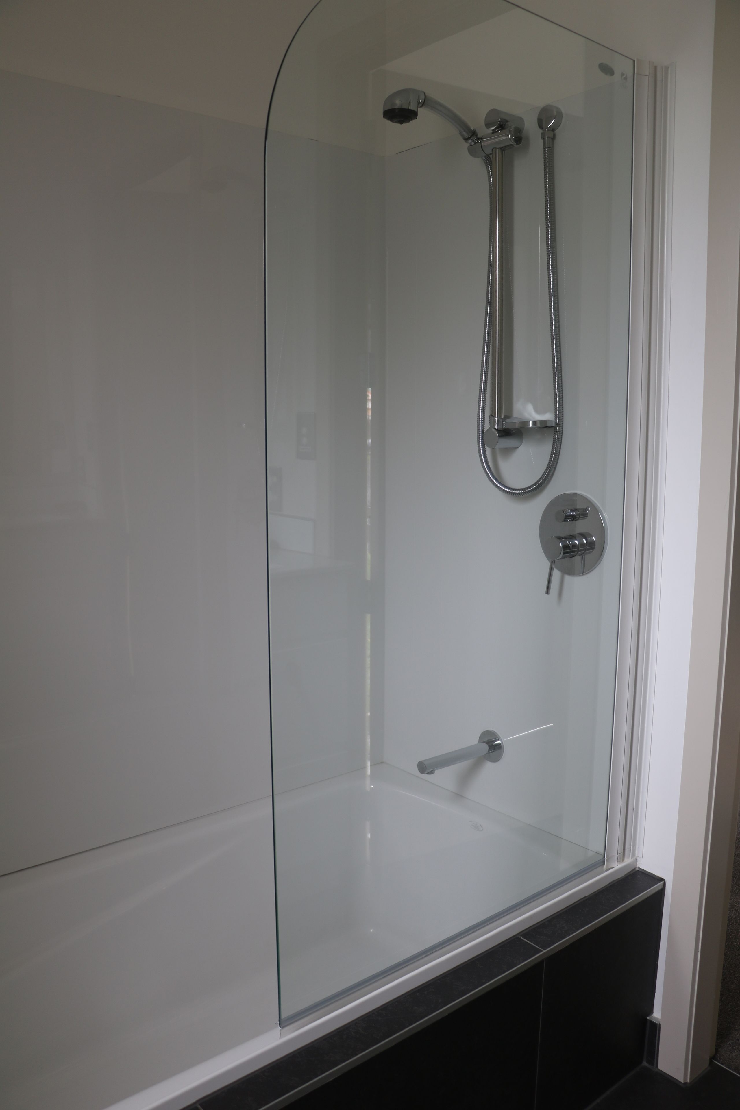 Un box de ducha moderno con puerta de cristal, un cabezal de ducha de mano y un grifo empotrado en la pared.