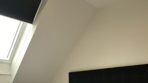 A neatly made bed with white linens and a grey patterned bedspread, a dark headboard, and a skylight above. - MCM Motel (Christchurch)