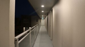 A corridor with a white railing, recessed lighting, and a view of buildings outside. - MCM Motel (Christchurch)