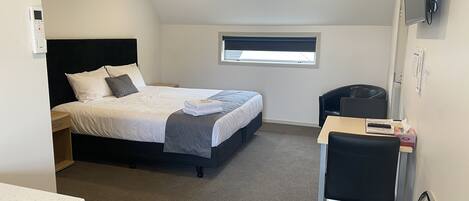 Una habitación de hotel compacta con una cama, un escritorio, una silla y un ventanal pequeño.