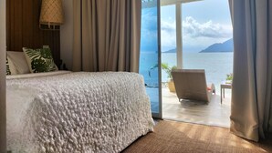 Un dormitorio con una cama grande, vistas al mar y un balcón con una silla.