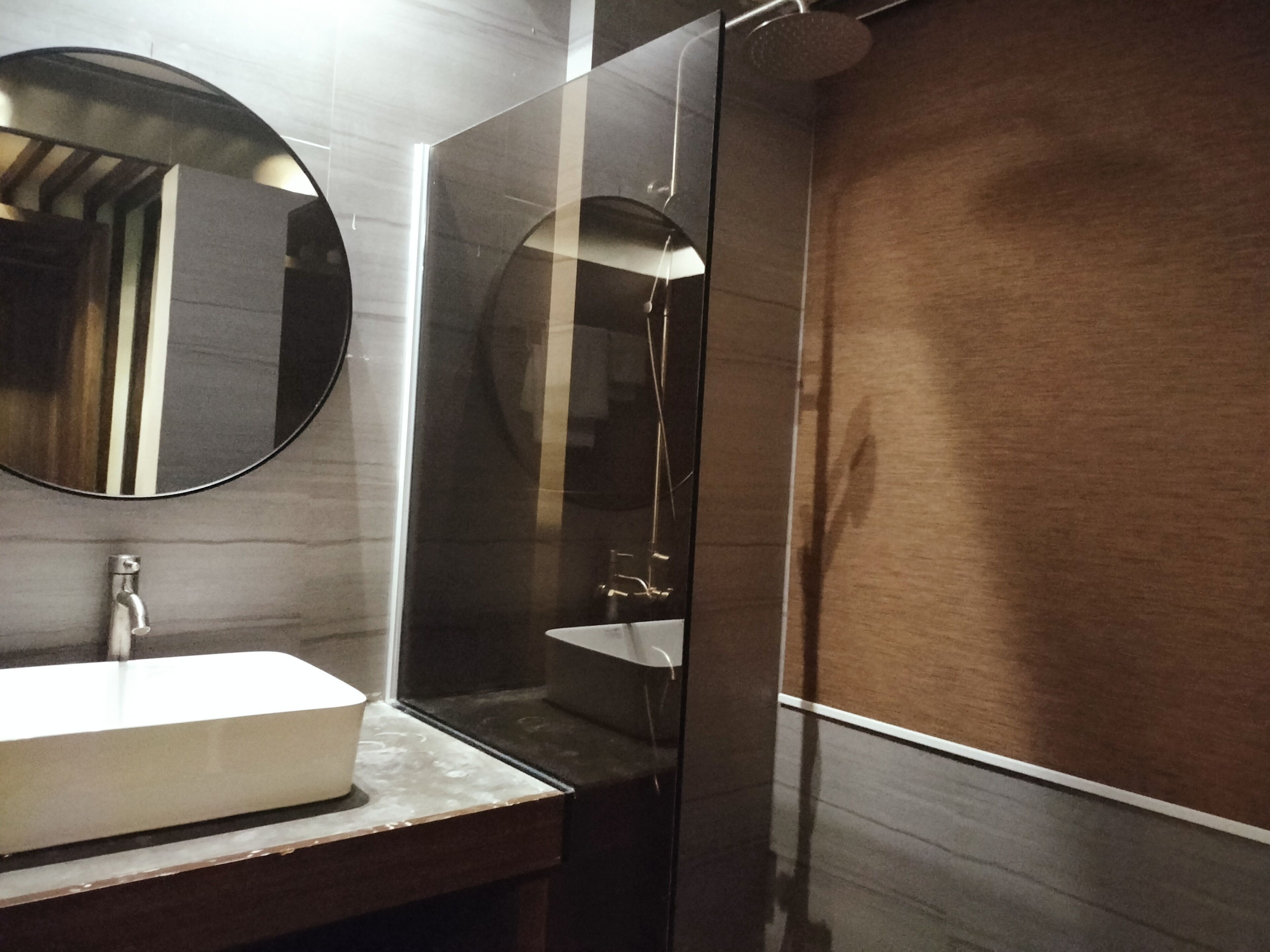 A modern bathroom with a rectangular sink, a round mirror, and a glass-enclosed shower.
