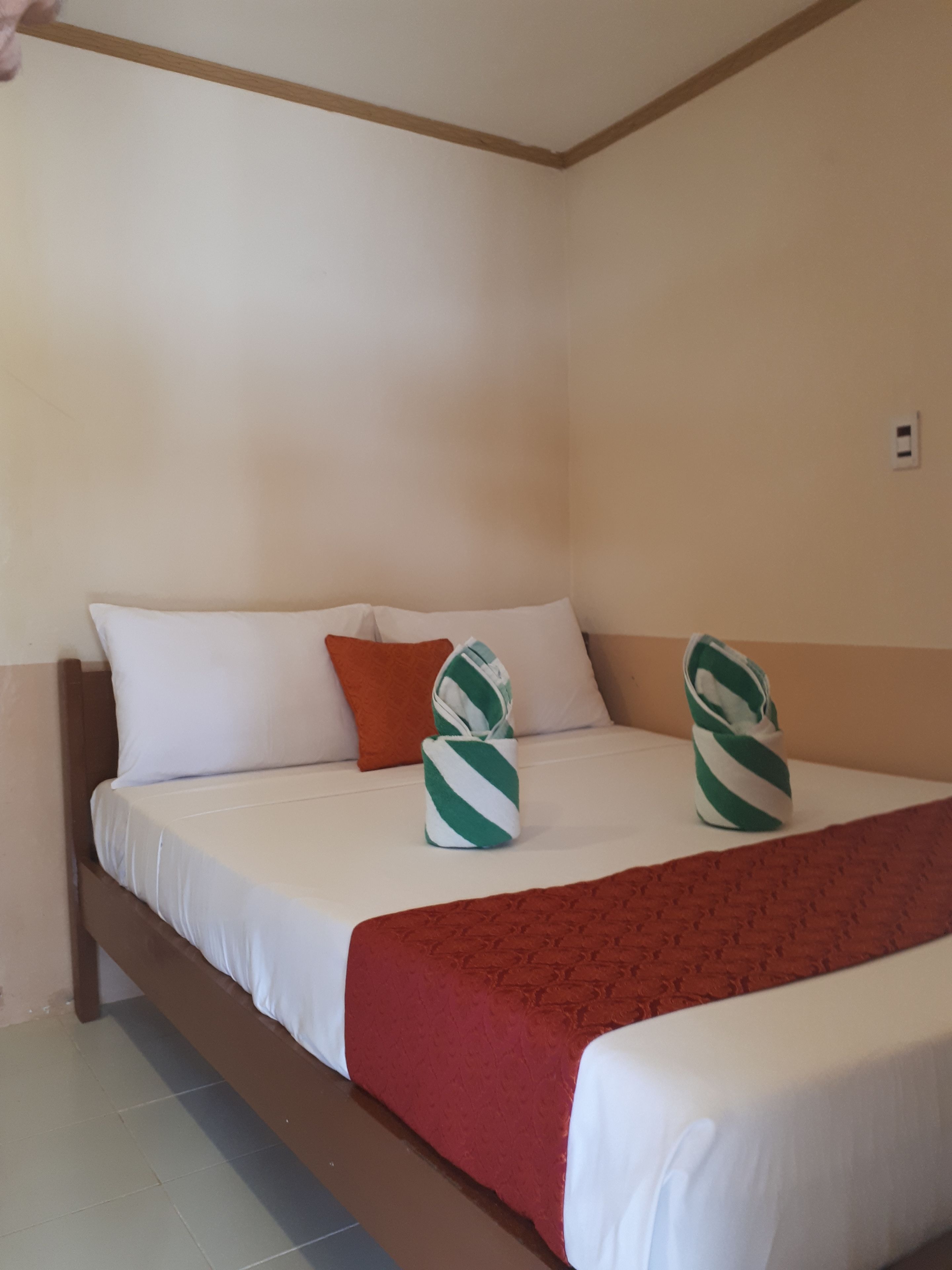 Una habitación de hotel con una cama, ropa blanca, una colcha roja y dos toallas a rayas verdes y blancas.
