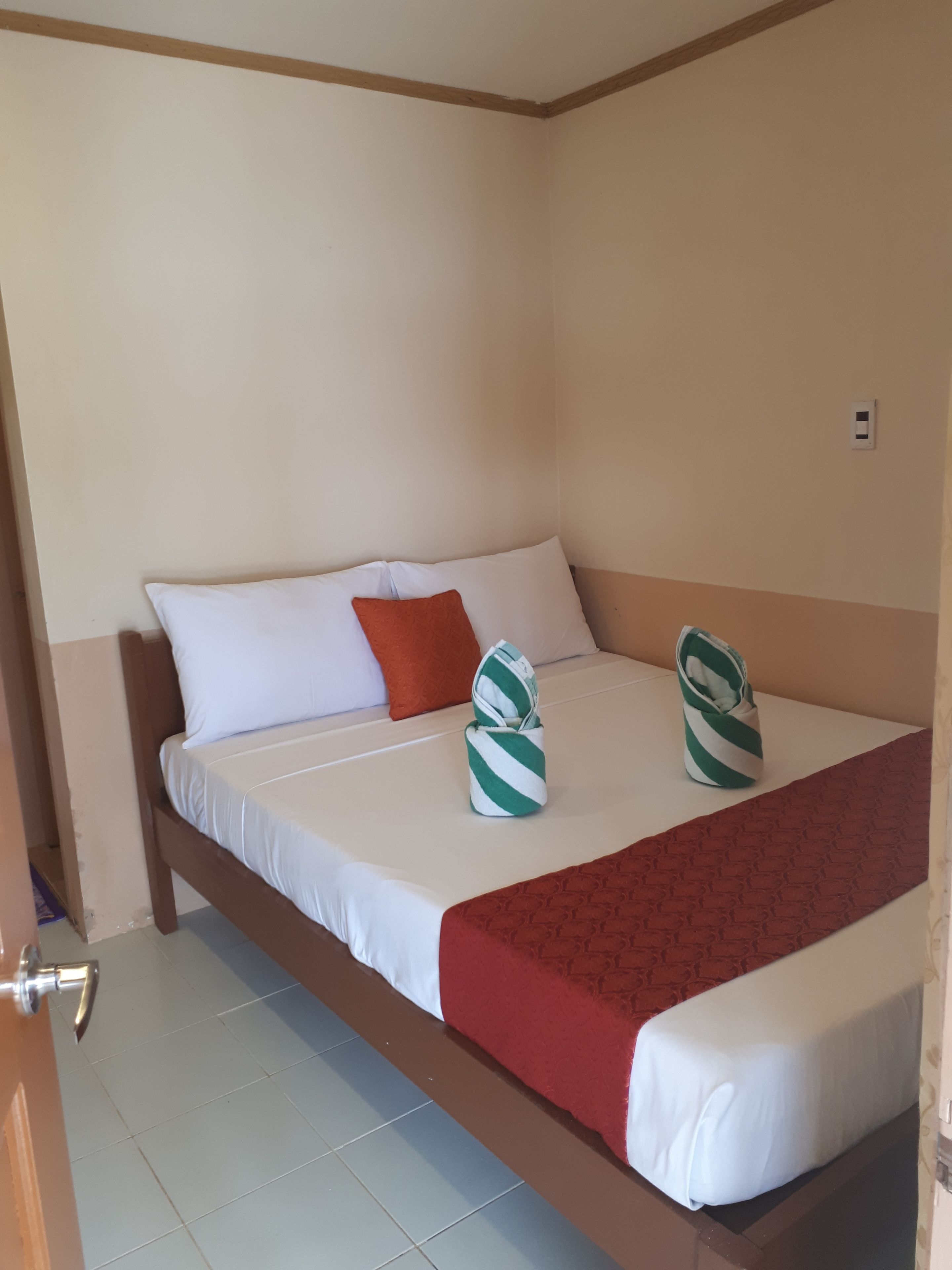 A hotel room with a bed, pillows, a red blanket, and a towel folded on the bed.