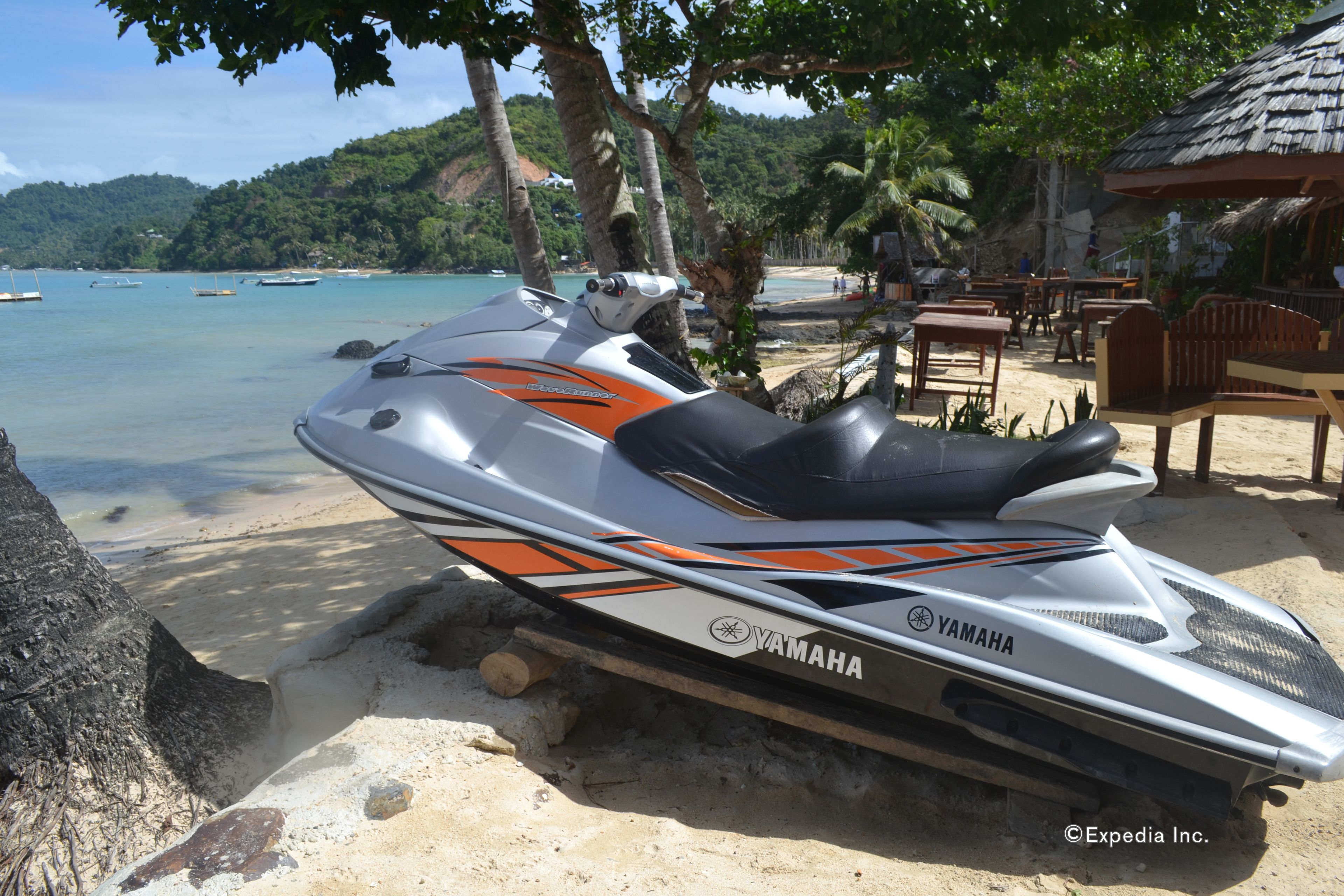 Een Yamaha jetski geparkeerd op een zandstrand, met uitzicht op de oceaan en een rieten hutje op de achtergrond.