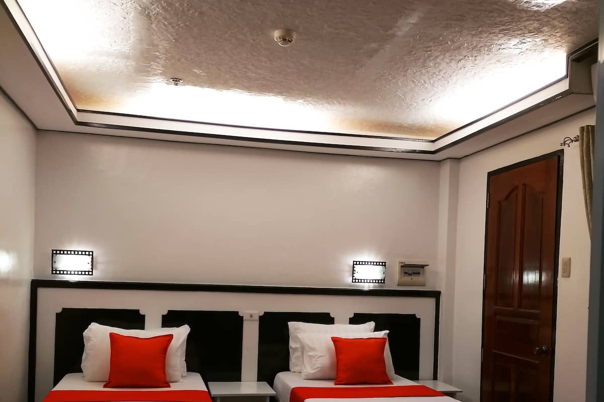 Ein Zimmer mit zwei Betten, jeweils mit weißer Bettwäsche und roten Kissen, einem kleinen Tisch und einer Deckenleuchte.