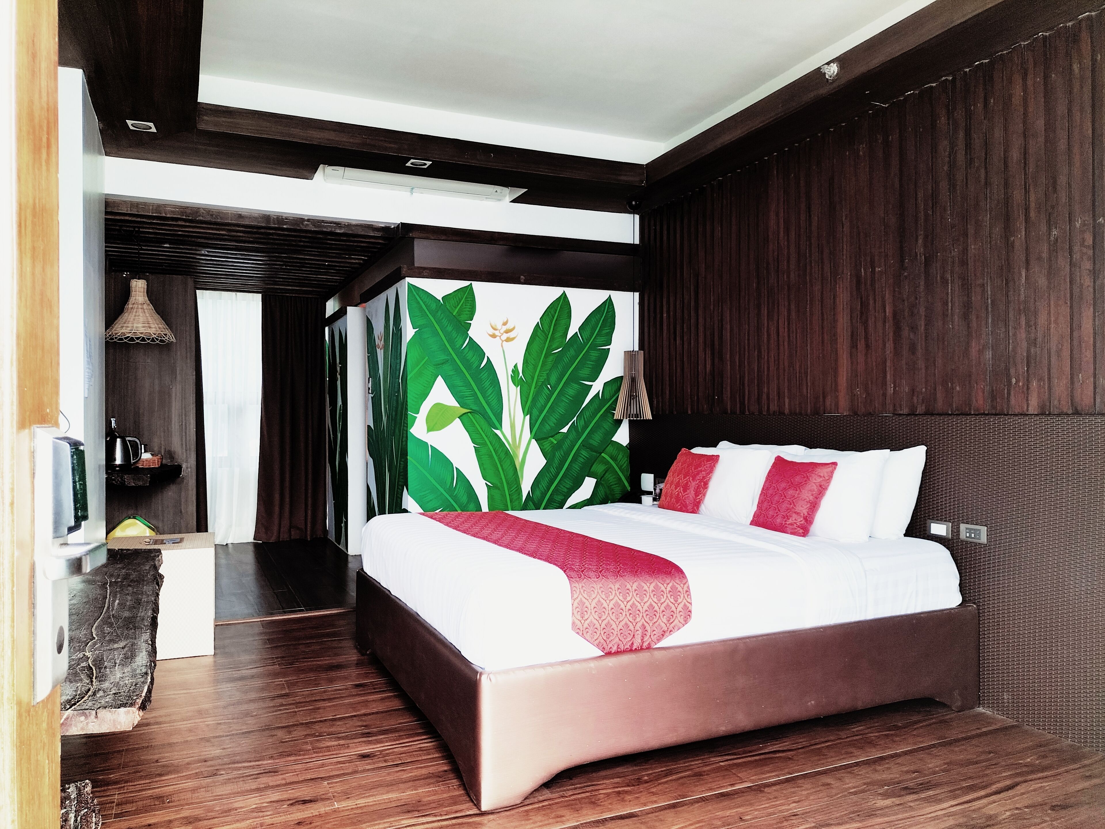 Una camera d'albergo moderna con un letto grande, pavimento in legno e parete decorata con un motivo a foglia tropicale.