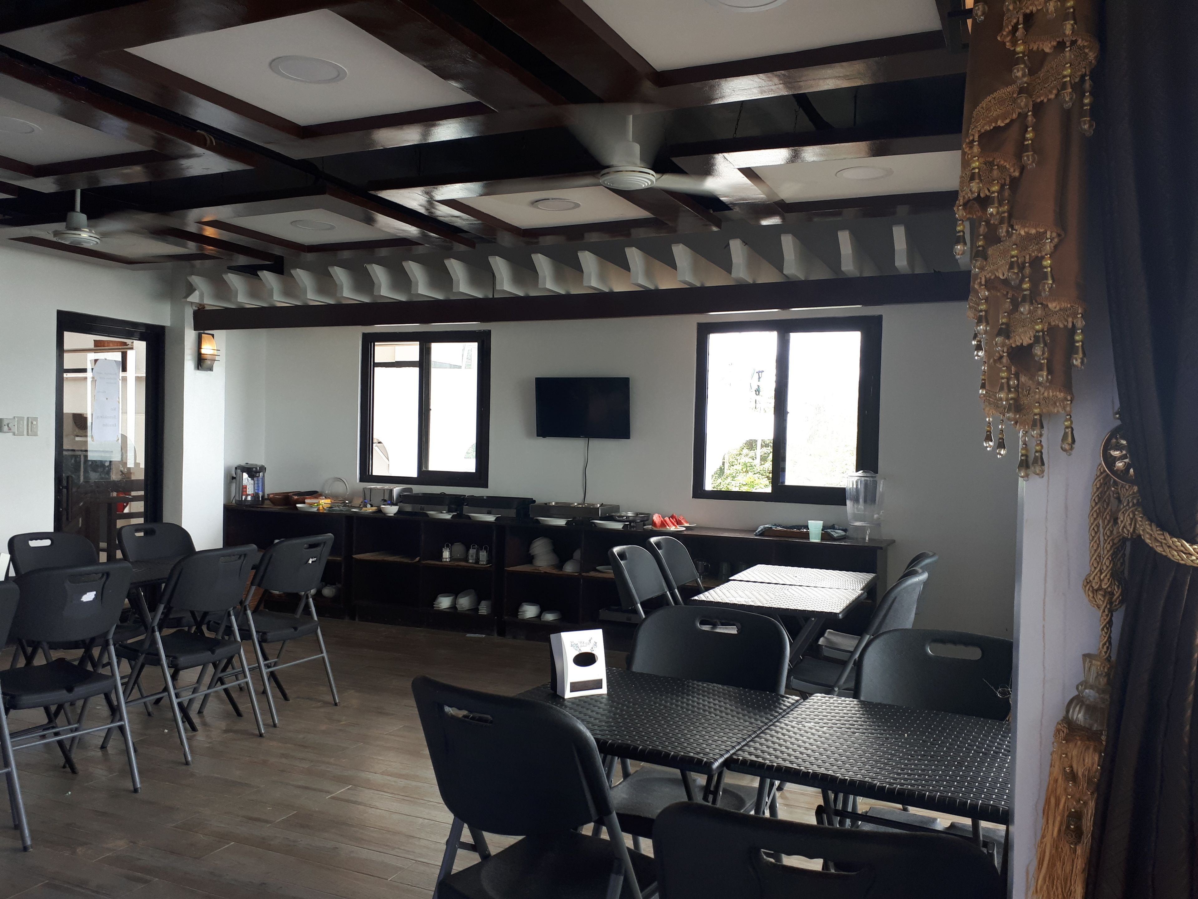 A restaurant with a high ceiling, exposed beams, and a bar area. There are tables and chairs arranged for dining.