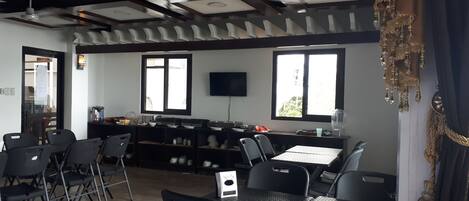 A restaurant with a high ceiling, exposed beams, and a bar area. There are tables and chairs arranged for dining.