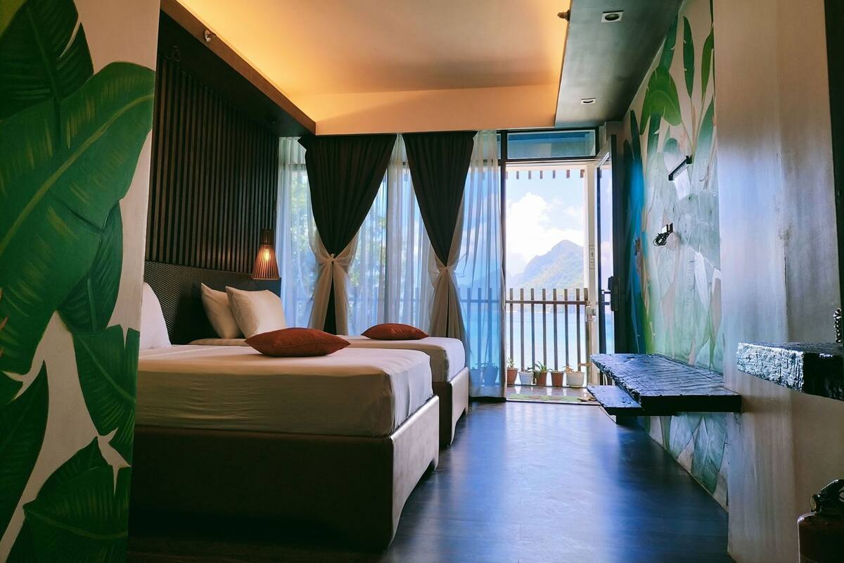 Ein Hotelzimmer mit Bett, kleinem Tisch, Meerblick und einem Balkon mit Geländer.