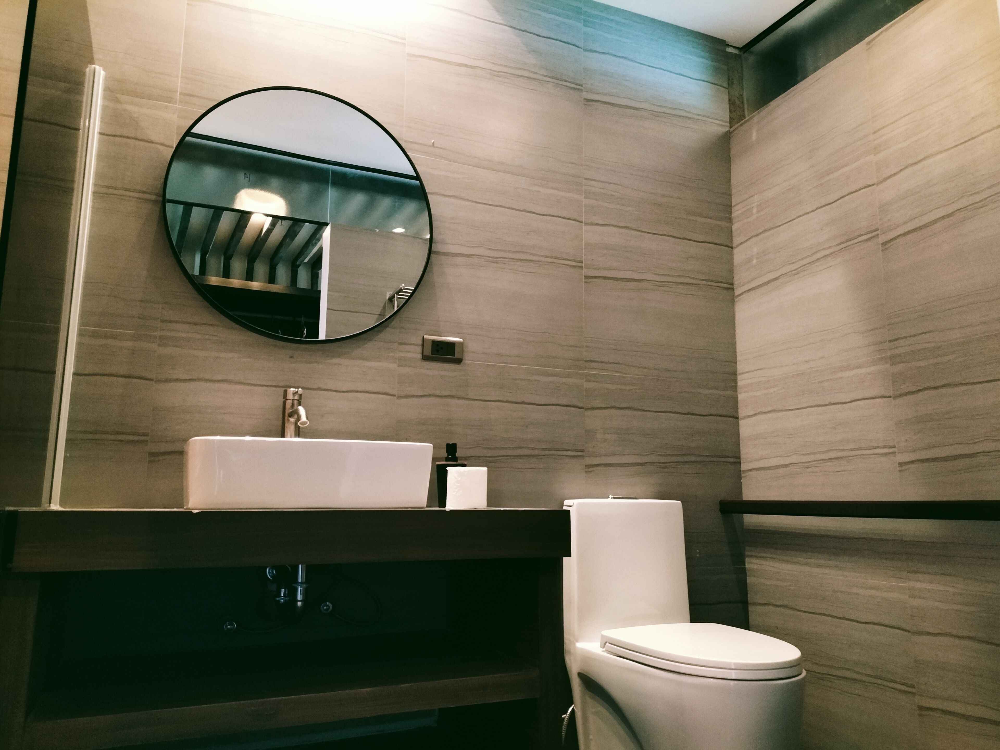 Un baño moderno con un espejo redondo, un lavabo y un inodoro.