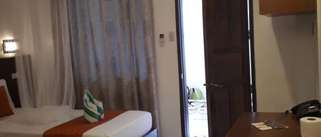A hotel room with two beds, a small kitchenette, a bathroom, and a view of the outside.