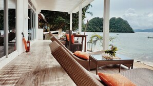 Un espacio de estar techado al aire libre con mobiliario de mimbre y vista al mar.