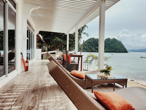 A covered outdoor seating area with wicker furniture and a view of the sea.