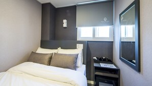 A modern hotel room with a neatly made bed, a bedside table with a lamp, a mirror, and a window with blinds. - Philstay Myeongdong Metro (Seoul)