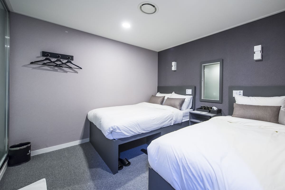 A hotel room with two beds, a small desk, a mirror, and a coat rack.