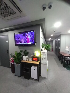 A modern office space with a flat-screen TV, a small desk with a computer, a trash bin, and a refrigerator.