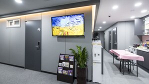 A modern reception area with a flat-screen TV displaying a painting, a plant, a bulletin board, and a small kitchenette. - Philstay Myeongdong Metro (Seoul)