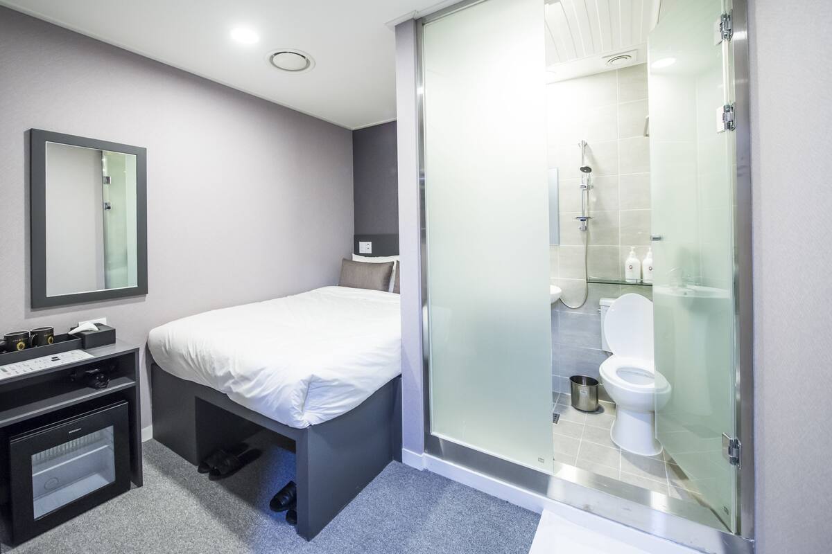 A modern bathroom with a glass shower enclosure, a toilet, and a bed with a bedside table.