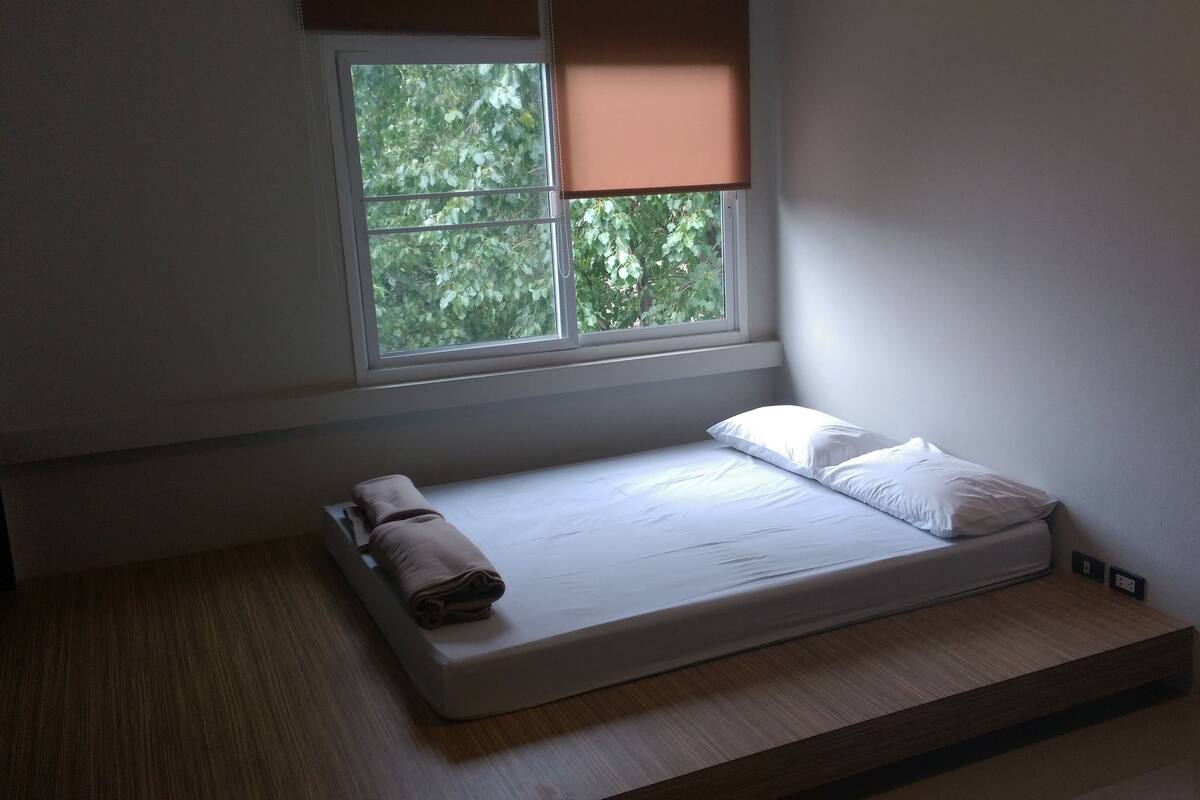 A small, single-bed room with a window, a mattress, and a pillow.