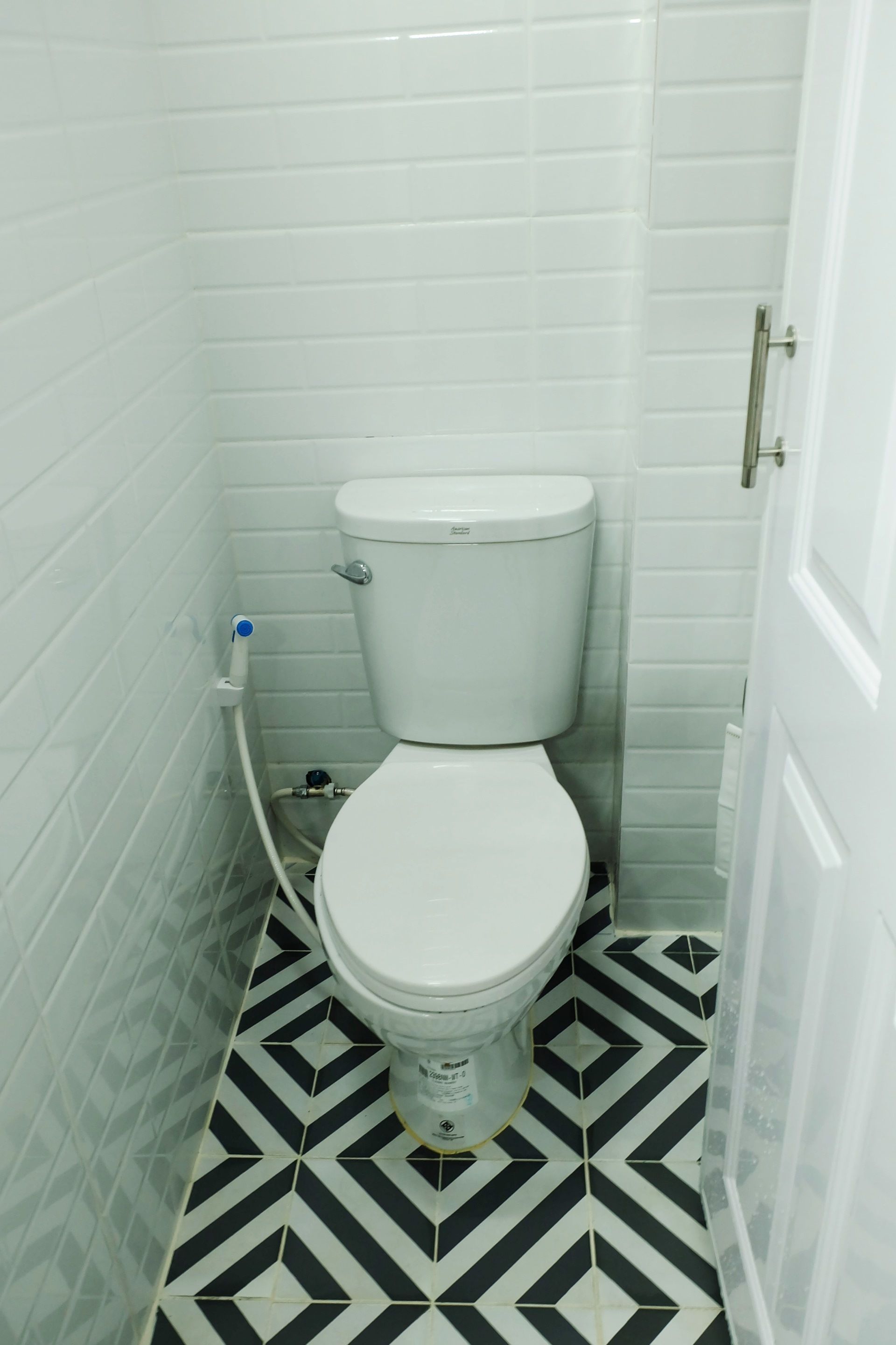 A small bathroom with a white toilet, a black and white patterned floor, and white tiled walls.