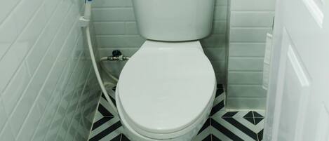 A small bathroom with a white toilet, a black and white patterned floor, and white tiled walls.