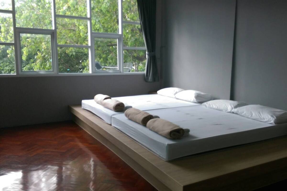A single bed with white linens and two rolled towels, a wooden platform, and a window with a view of trees.