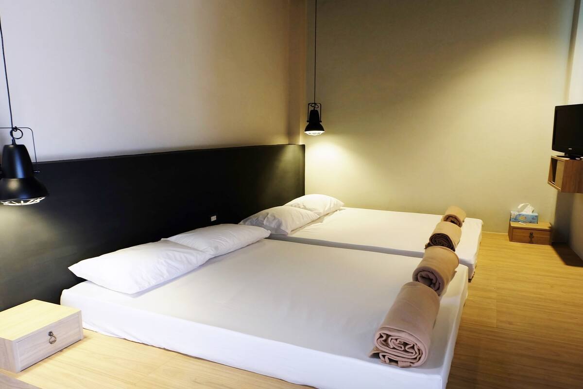A double bed with white linens, two bedside lamps, a wooden nightstand with a drawer, and a small wooden box.