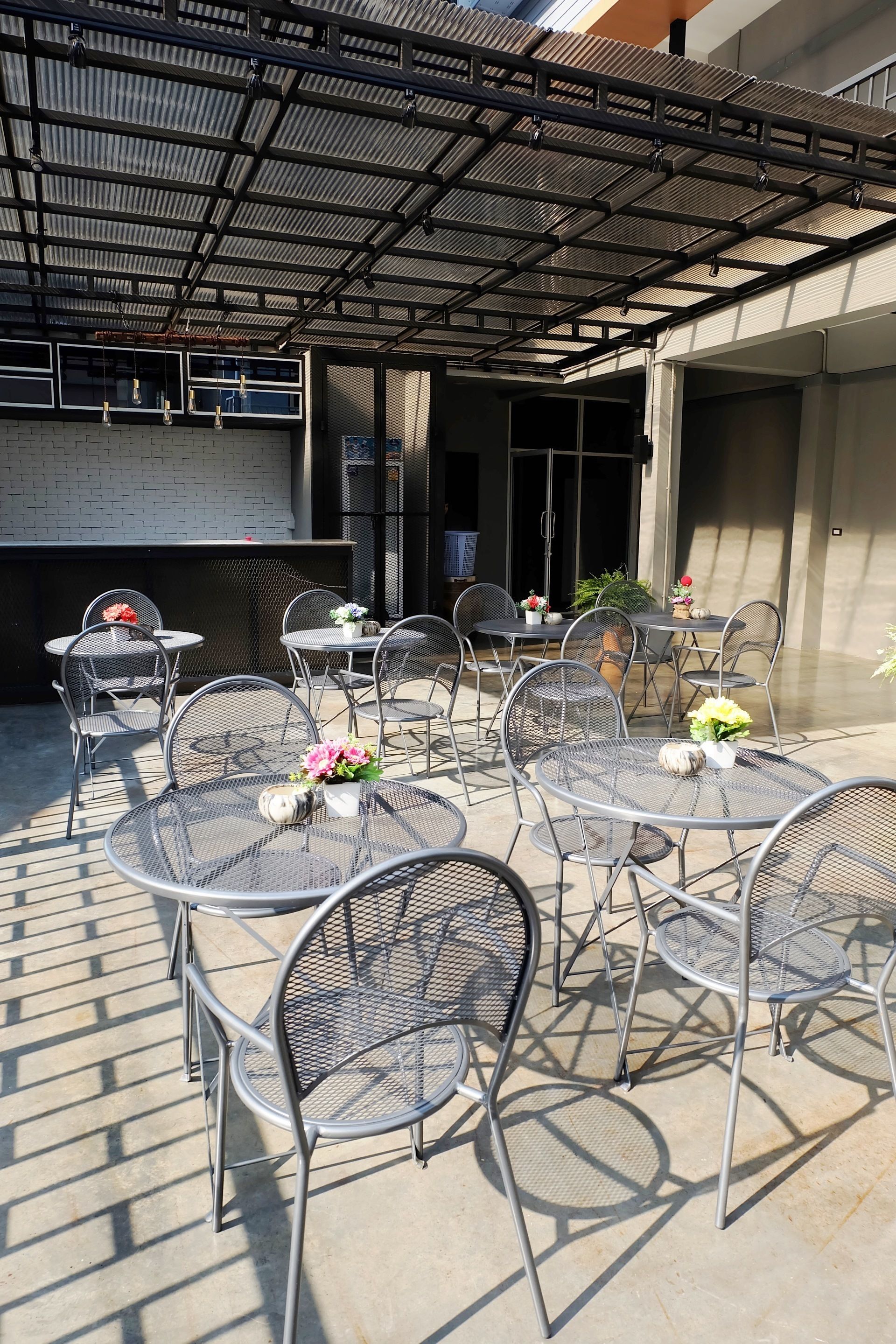 Un patio al aire libre con mesas y sillas de metal, algunas decoradas con flores.