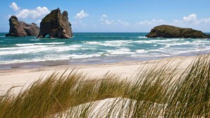 A beach with clear blue water, rocky formations, and grassy dunes.