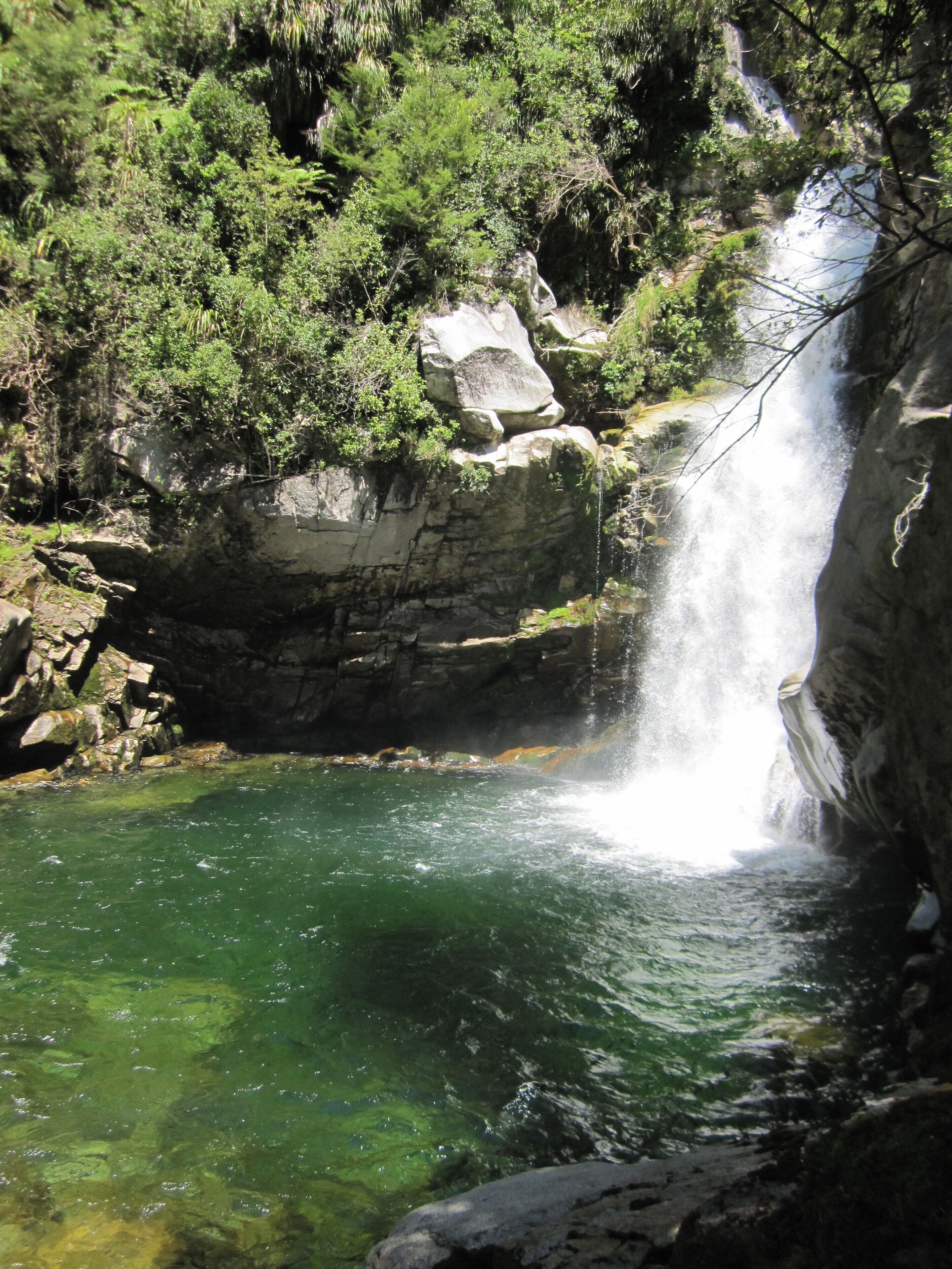 Une cascade se jetant dans un bassin d’eau claire, entouré d’un paysage rocheux et d’une végétation luxuriante.