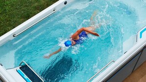 A person swimming in a rectangular hot tub with a built-in seat and steps on the side.
