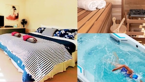 A bedroom with a bed, a bedside table, and a painting. There is also a wooden bench with towels and a fan.
