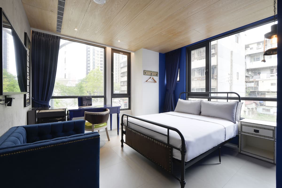 A bedroom with a bed, bedside tables, a chair, and large windows offering a view of buildings.