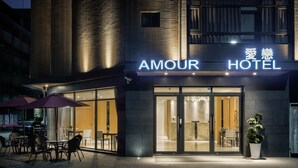Das Äußere des Amour Hotels mit moderner Fassade, großem Glasanbau und Außenbereich mit Sonnenschirmen.