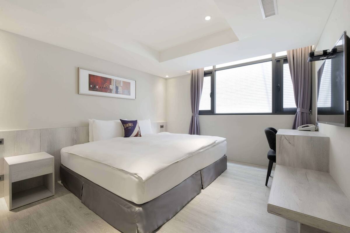 A modern hotel room with a large bed, a desk, and a window with curtains.