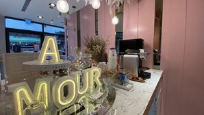 Ein Hotel-Rezeptionsbereich mit Marmor-Theke, leuchtendem 'A MOUR' Schild, dekorativer Beleuchtung und einer Kaffeemaschine.