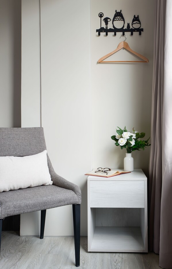 Una habitación moderna con un sillón gris, una mesita de noche blanca con un florero de flores blancas y un adorno temático de gatos negros montado en la pared.