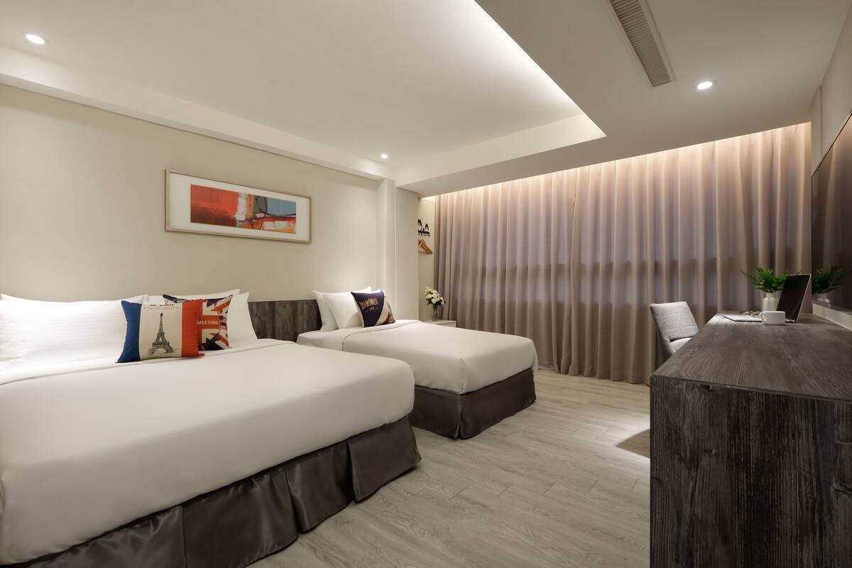 A modern hotel room with two beds, a desk, and a large window with curtains.