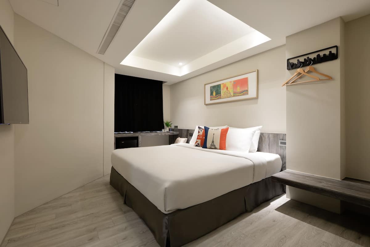 A modern hotel room with a large bed, a desk, and a hanging coat rack.
