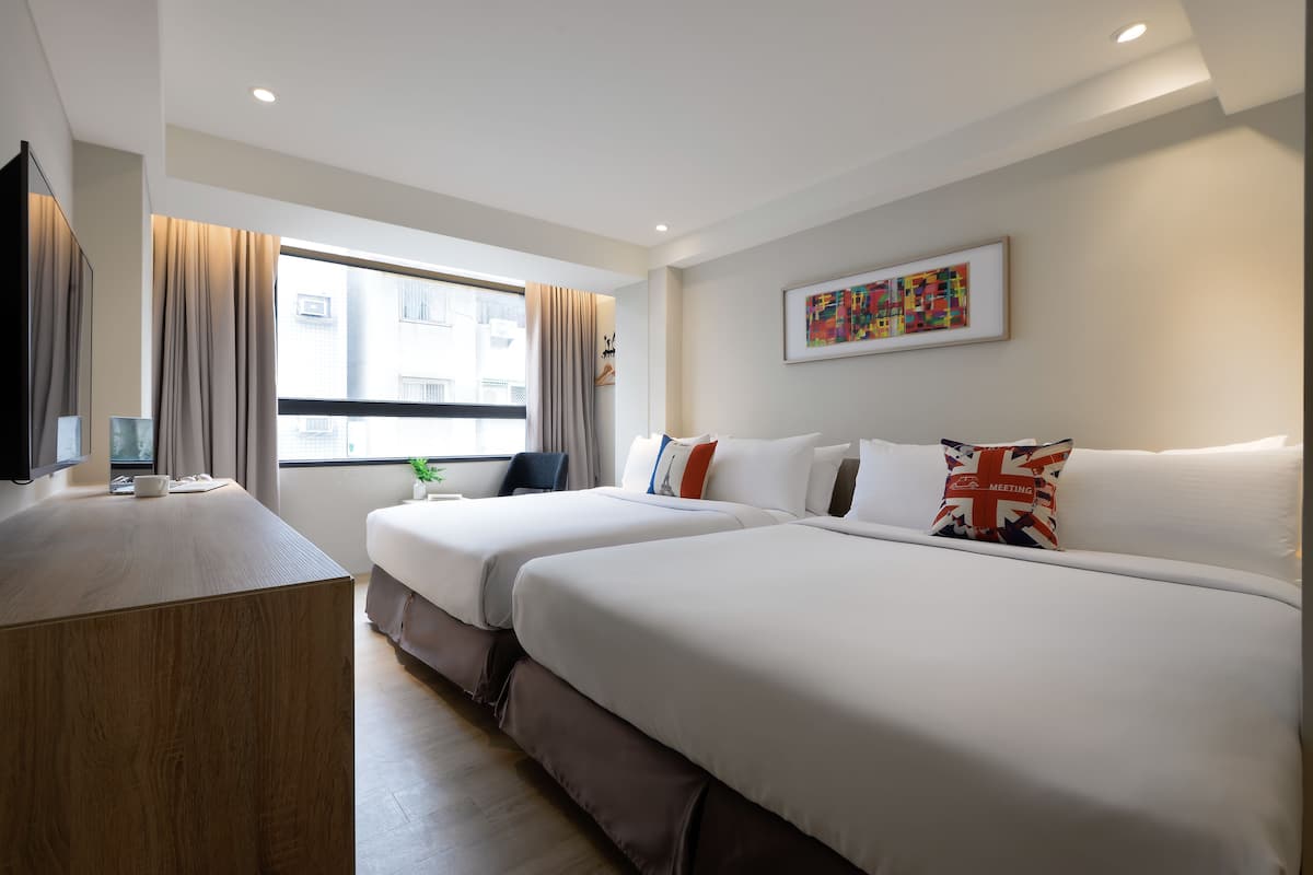 A hotel room with two beds, a desk, a window with curtains, and a painting on the wall.